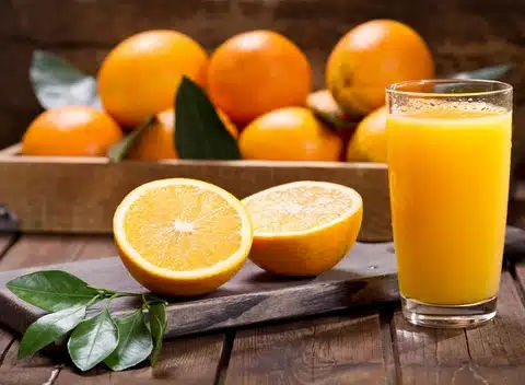 Drinks For Cholesterol That You Should Add In Your Diet Today ! - Drinks to Lower Cholesterol 13 An image of Stanol or sterol-fortified orange juice. Juice is served in glass and fresh and ripe orange are cut in half on the side on chopper. There's also a small leaf branch on the chopper and there are many more bright saffron out-focused or blurred oranges on the back in a wooden container.