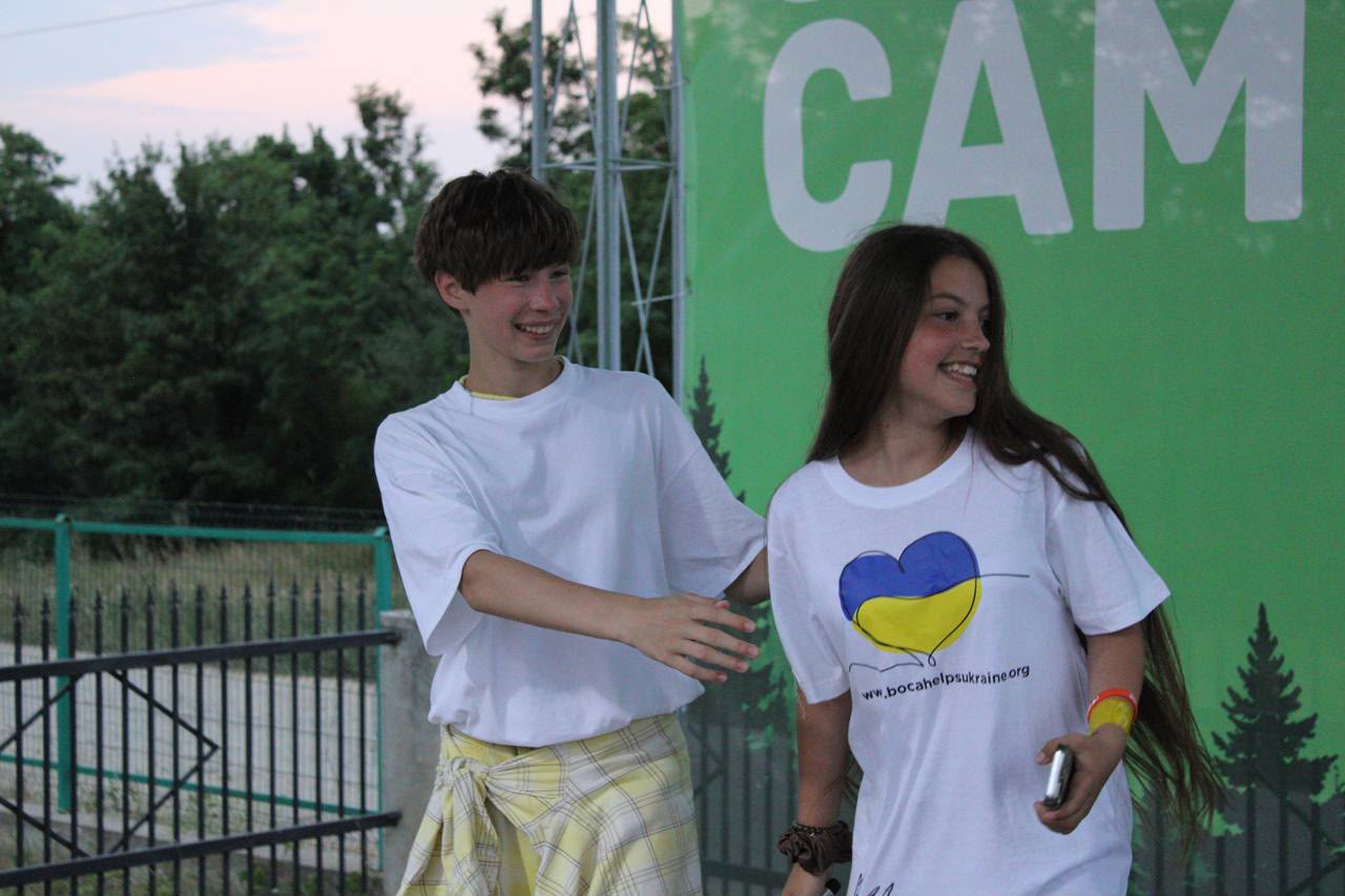 Two camp participants smiling beside the camp sign
