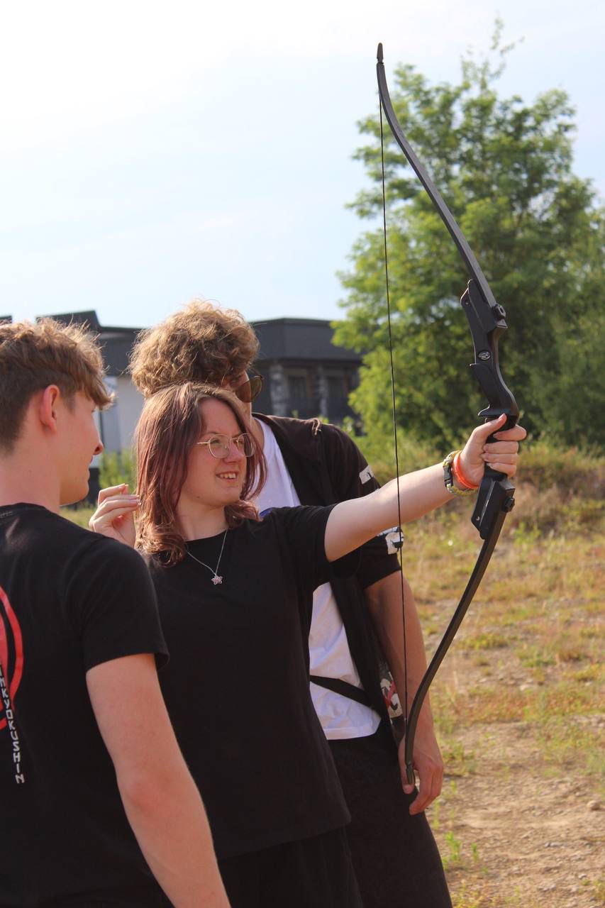 A camp participant practicing archery with others nearby