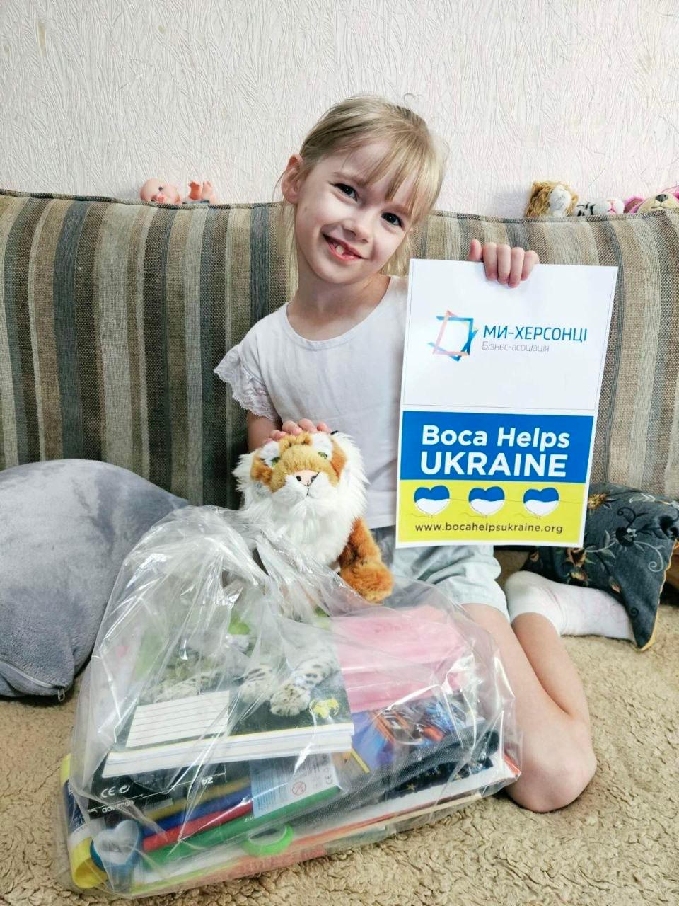 A child holding a Boca Helps Ukraine sign beside school supplies