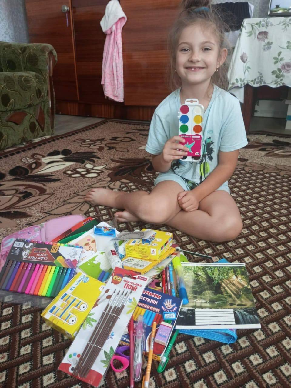A child sitting beside a collection of new school supplies