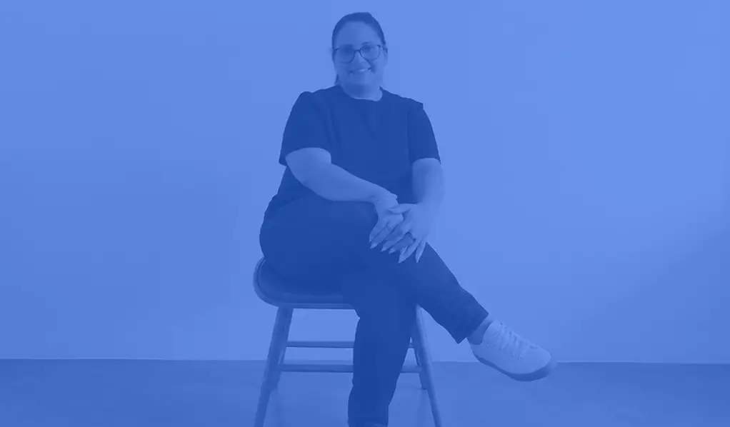 an image of Romina form Rokitsite sitting on a chair with a medium blue coloured overlay