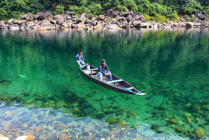 Two travellers in a wooden boat appearing to float above the transparent Umngot River at Dawki