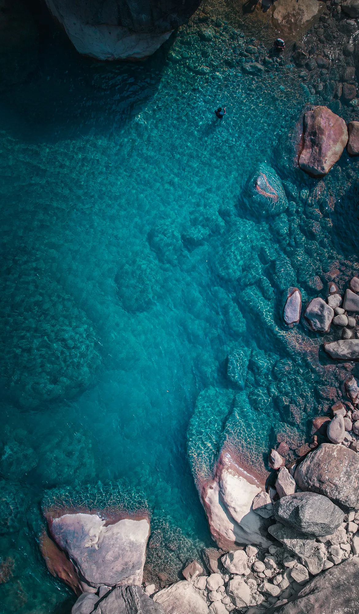 Aerial view of swimmers in the clear turquoise waters of the Umngot River among sandstone rocks