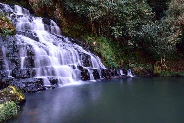 A multi-tiered waterfall cascading into a green pool near Cherrapunji