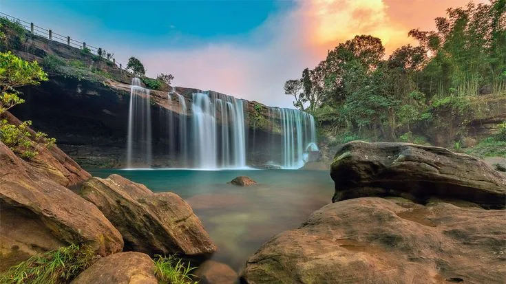 A waterfall spilling into a turquoise pool at sunset in Meghalaya