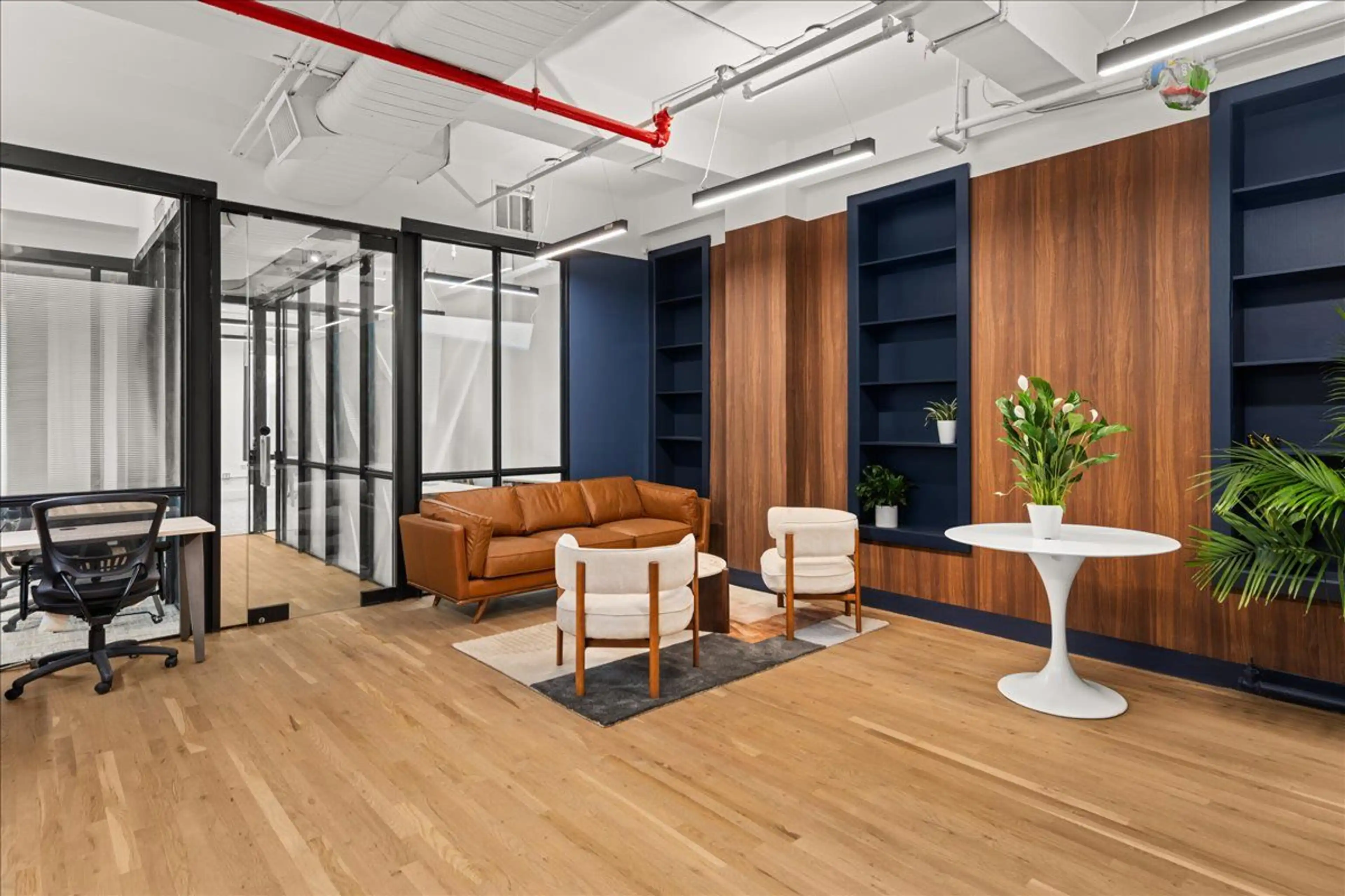 Flatiron coworking suite with tan leather sofa, white chairs, and greenery for a refined look.