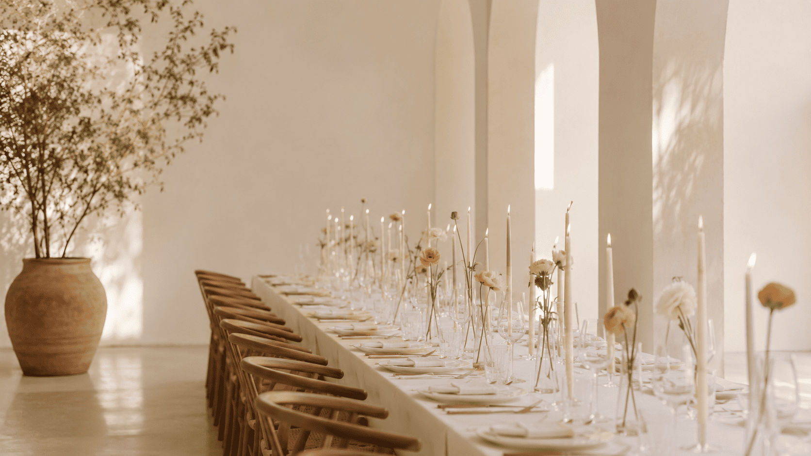 Boda minimalista moderna con mesa larga de mantel blanco liso, un solo tallo floral por comensal, velas delgadas y espacio arquitectónico limpio y luminoso