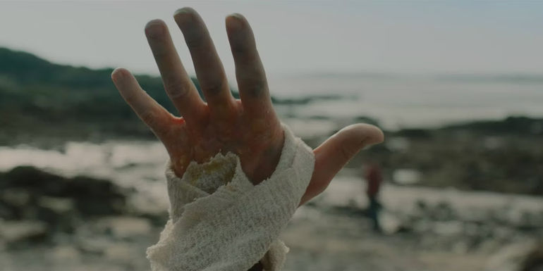 A bandaged hand thrust into the sky on the beach in a short film adaptation of I Am The Doorway