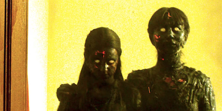 Two badly burned ghosts stare at the camera angrily in We Are Still Here