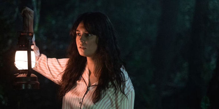 Lottie (Courtney Eaton) holdding a lamp in the dark woods alone in Yellowjackets season 1 episode 6 Saints.