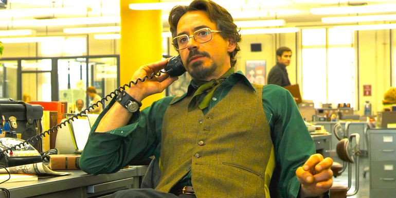 Robert Downey Jr's Paul Avery in 70s garb talking on the phone in a bustling newsroom in Zodiac