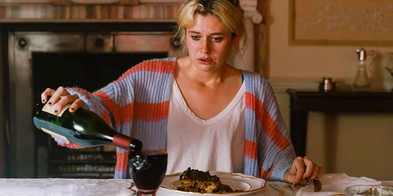 Venetia Catton (Alison Oliver) looking deeply disturbed while pouring wine into an overflowing glass in Saltburn.