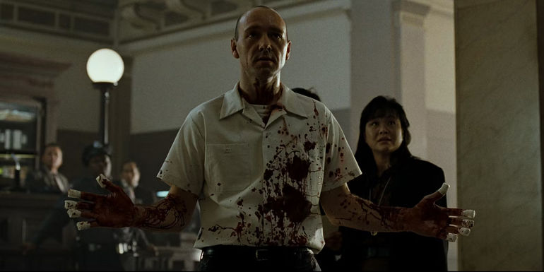 A bloodied John Doe raises his hands in Se7en