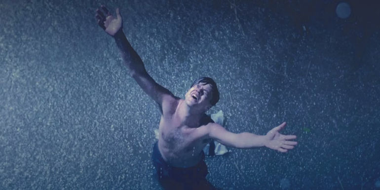 Tim Robbins as Andy Dufresne stands with his arms raised to the sky in the rain in The Shawshank Redemption.