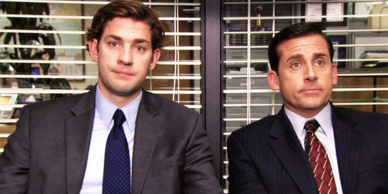 2-51Steve Carell as Michael Scott sitting with John Krasinski as Jim Halpert in The Office as both men look serious in suits