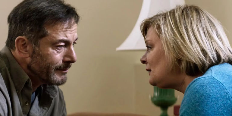 Jason Isaacs and Martha Plimpton sit across from each other in tears in the film Mass