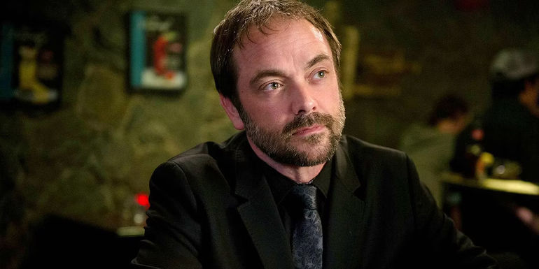 Crowley (Mark Sheppard) sitting at a table in Supernatural