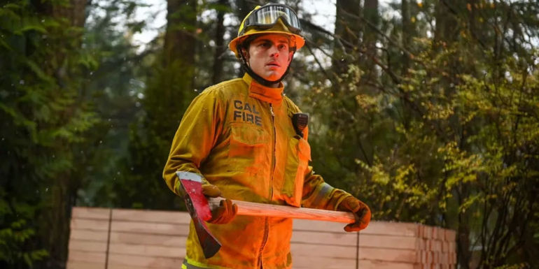 Alex Shawcross (Zach Tinker) hilding an ax and wearing a fireman's unifrom in the forest in Fire Country.