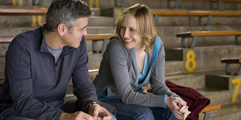 George Clooney and Vera Farmiga laughing on bleachers in Up in the Air