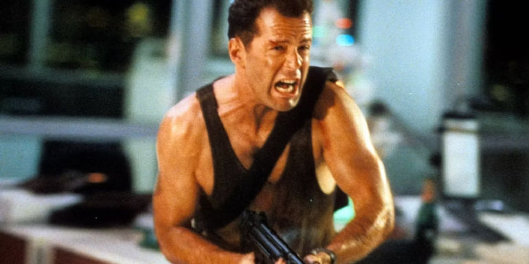 Bruce Willis as John McClane shouting and running while holding a gun in Die Hard.