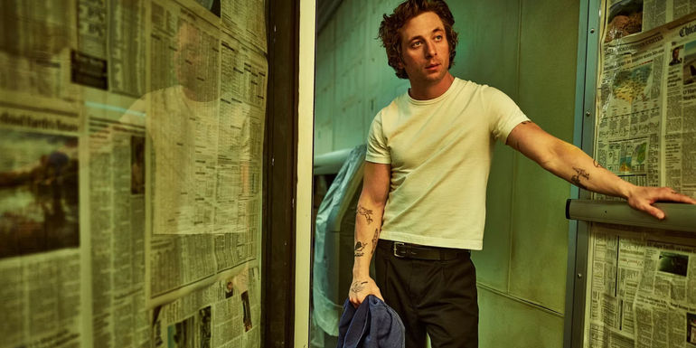 Carmy standing in a doorway where the glass door and window is covered in newspapers in The Bear