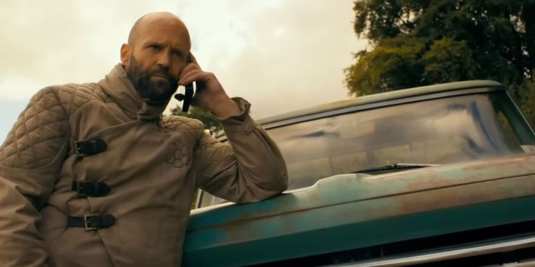 Jason Statham as Clay from The Beekeeper leaning against the hood of a truck talking on a phone