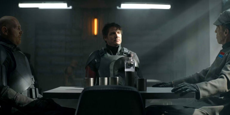Pedro Pascal as Din Djarin sits with Migs Mayfeld and Valin Hess in the Imperial mess hall on Morak in The Mandalorian season 2, episode 7