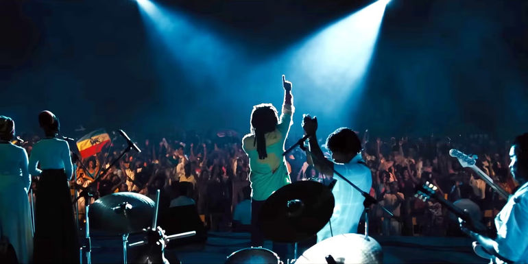 A still of Kingsley Ben-Adir as Bob Marley pointing his finger to the sky while performing onstage in Bob Marley: One Love