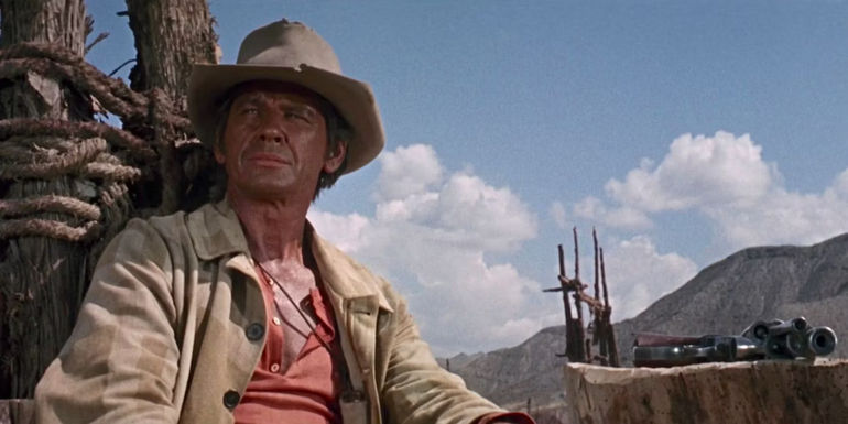 Charles Bronson as Harmonica gazes off into the distance with his revolver atop a tree stump in Once Upon a Time in the West