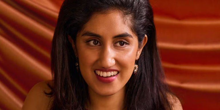 Emma smiles in front of an orange drapery in One Day.