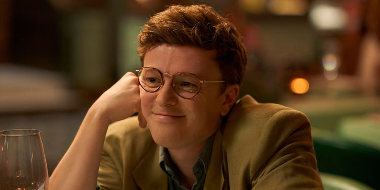 Ian smiles with his hand against his face in One Day