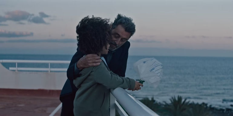 Ian McShane talks to a child while leaning against a railing in American Star