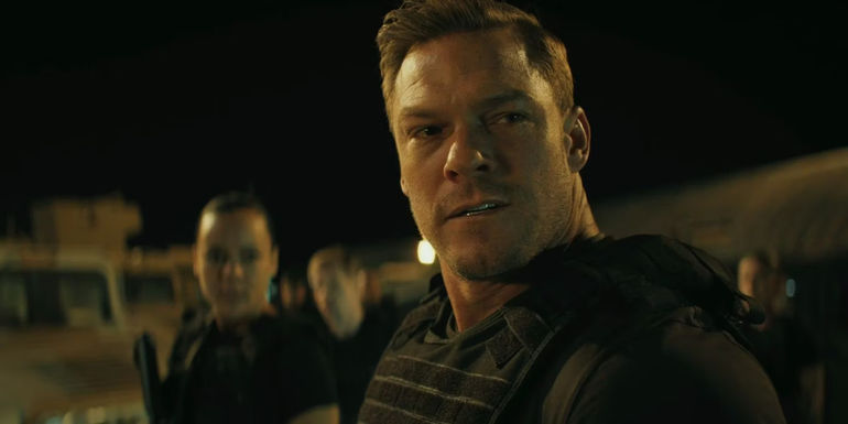 Alan Ritchson as Reacher wearing a bulletproof vest looking troubled