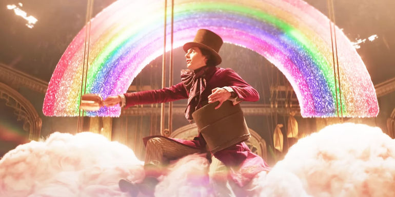 Timothée Chalamet sitting on a cloud as Wonka with a rainbow behind him.