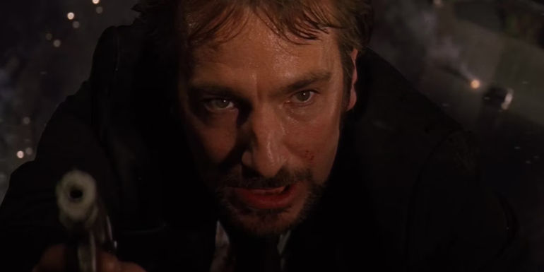Hans Gruber aiming a gun as he hangs out the window in Die Hard