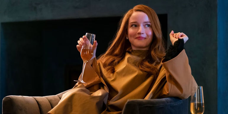 Julia Garner sits in a chair with a glass of wine in Inventing Anna