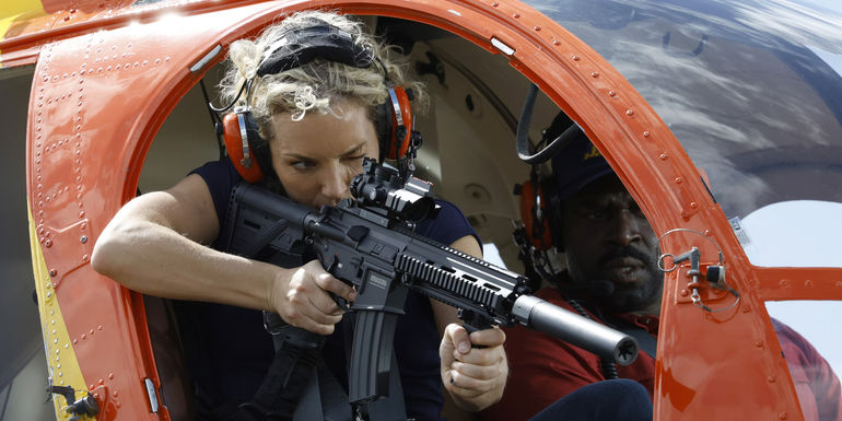 Magnum P.I.'s Higgins holding a machine gun leaning out of a helicopter.