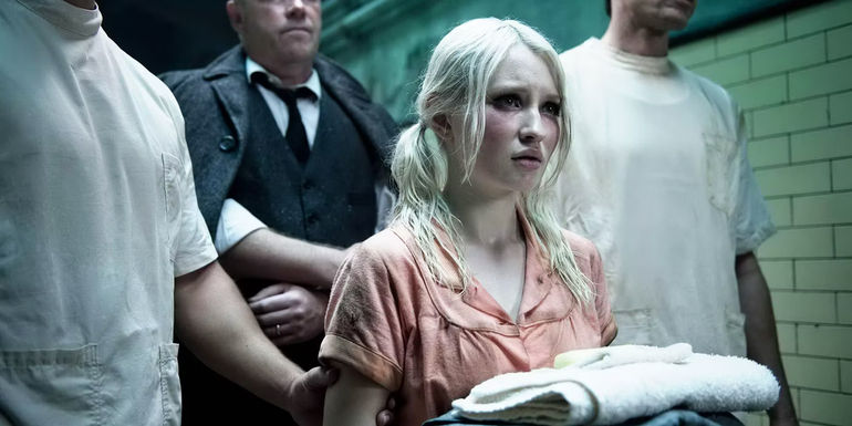 Emily Browning as Baby Doll with a folded towel in her hands being escorted by three men down a hallway in Sucker Punch.