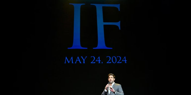 John Krasinski stands in front of a large screen announcing the release date for IF