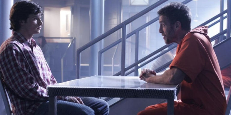 Tom Welling as Clark Kent and John Glover as Lionel Luther sitting across from each other over a prison table in Smallville