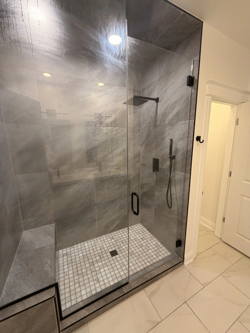 After -- frameless matte-black walk-in shower with tiled bench and marble mosaic pan at 456 W Briar Pl