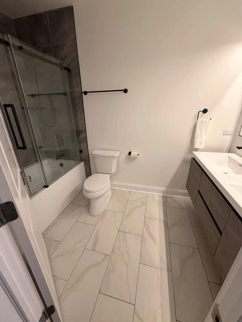 After -- guest bathroom with new tub, black-frame sliding glass and marble-look floors at 456 W Briar Pl