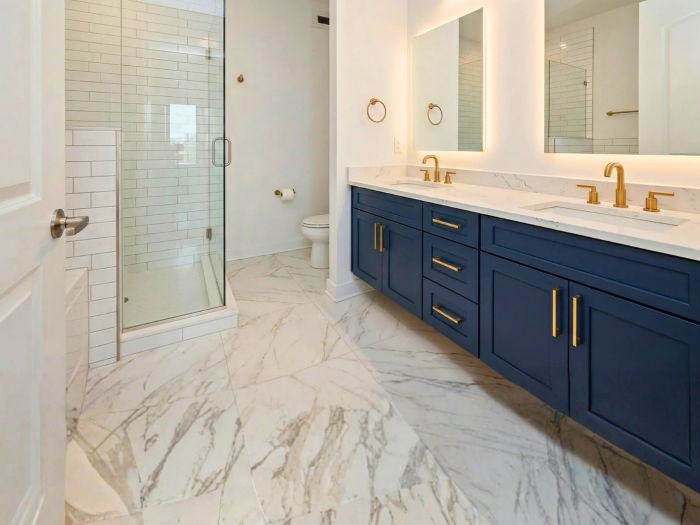 After bathroom renovation at The Chandler Condominiums Chicago -- navy floating vanity, backlit LED mirrors, Calacatta marble tile, frameless glass shower by Assembly Squad