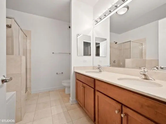 Before bathroom renovation at The Chandler Condominiums 450 E Waterside Dr Chicago -- builder-grade oak vanity, beige tile, Hollywood strip light