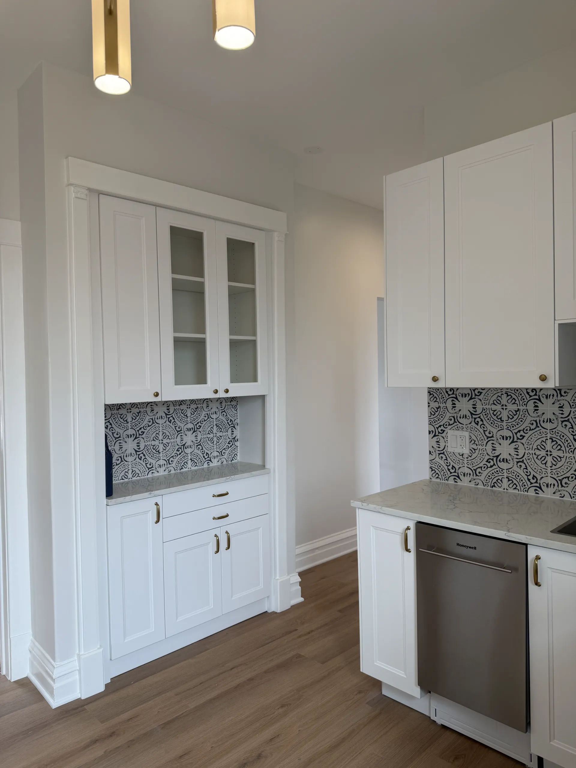 Custom built-in china cabinet with glass upper doors, brass hardware, quartz counter, and Moroccan tile backsplash in white shaker kitchen remodel Chicago