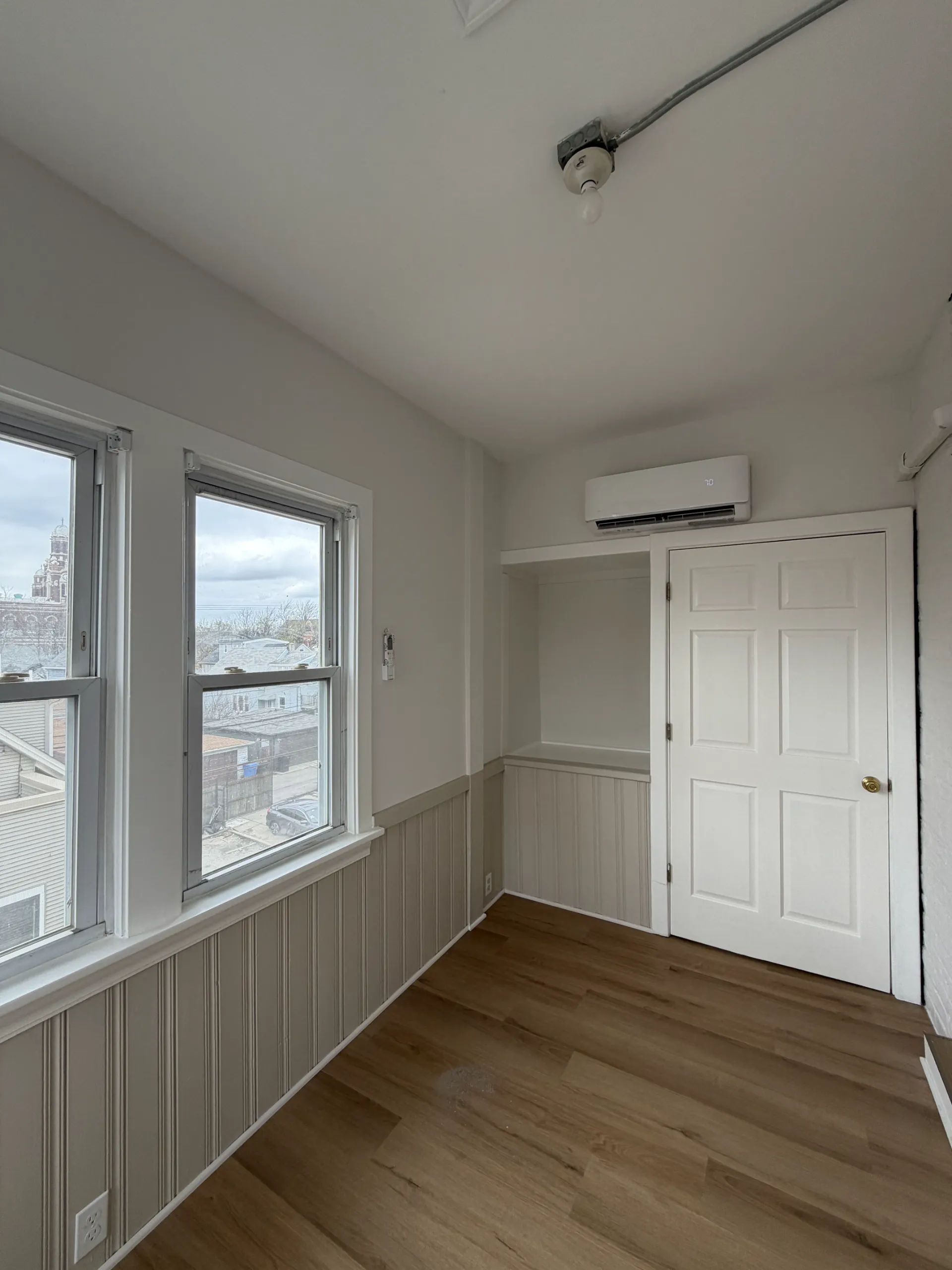 After photo of enclosed sunroom renovation with beadboard wainscoting, wood-look LVT flooring, corner windows, and ductless mini-split in Chicago Logan Square three-flat