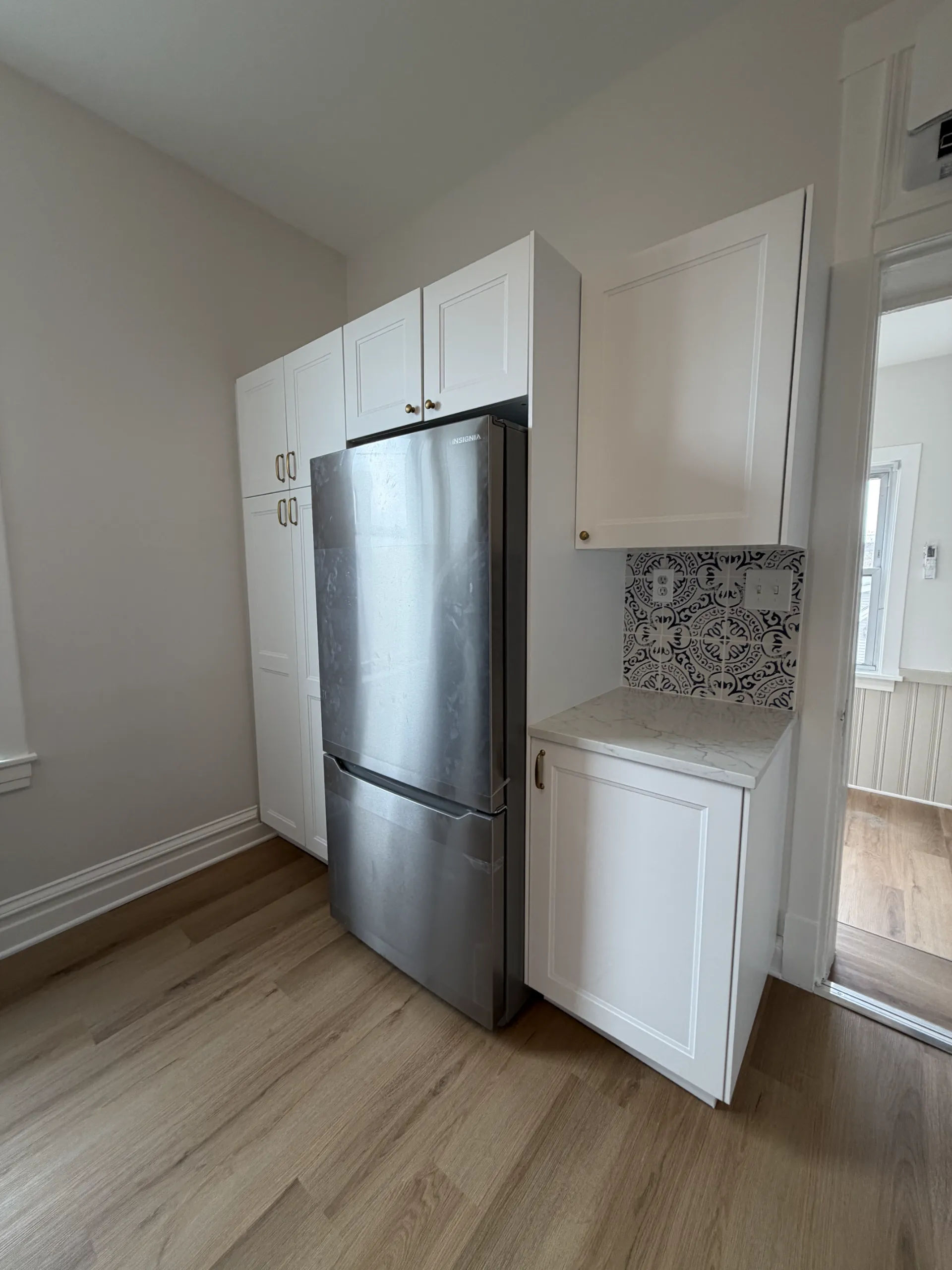 White shaker kitchen remodel with floor-to-ceiling tall pantry cabinets, Insignia stainless steel bottom-freezer refrigerator, and brass hardware in Chicago three-flat