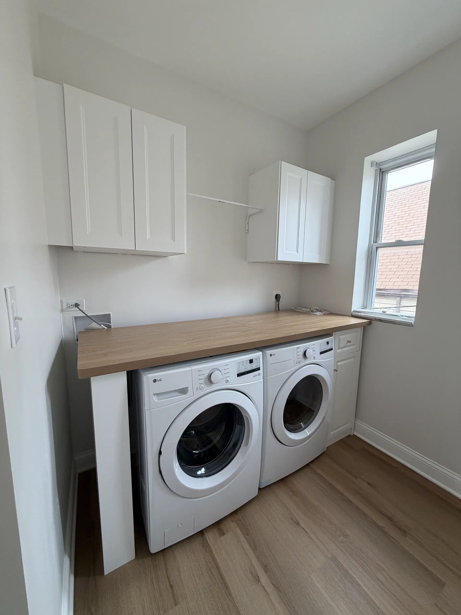After photo of laundry room remodel with side-by-side LG washer and dryer, butcher-block countertop, stacked white cabinets, and hanging rod in Chicago whole-unit renovation
