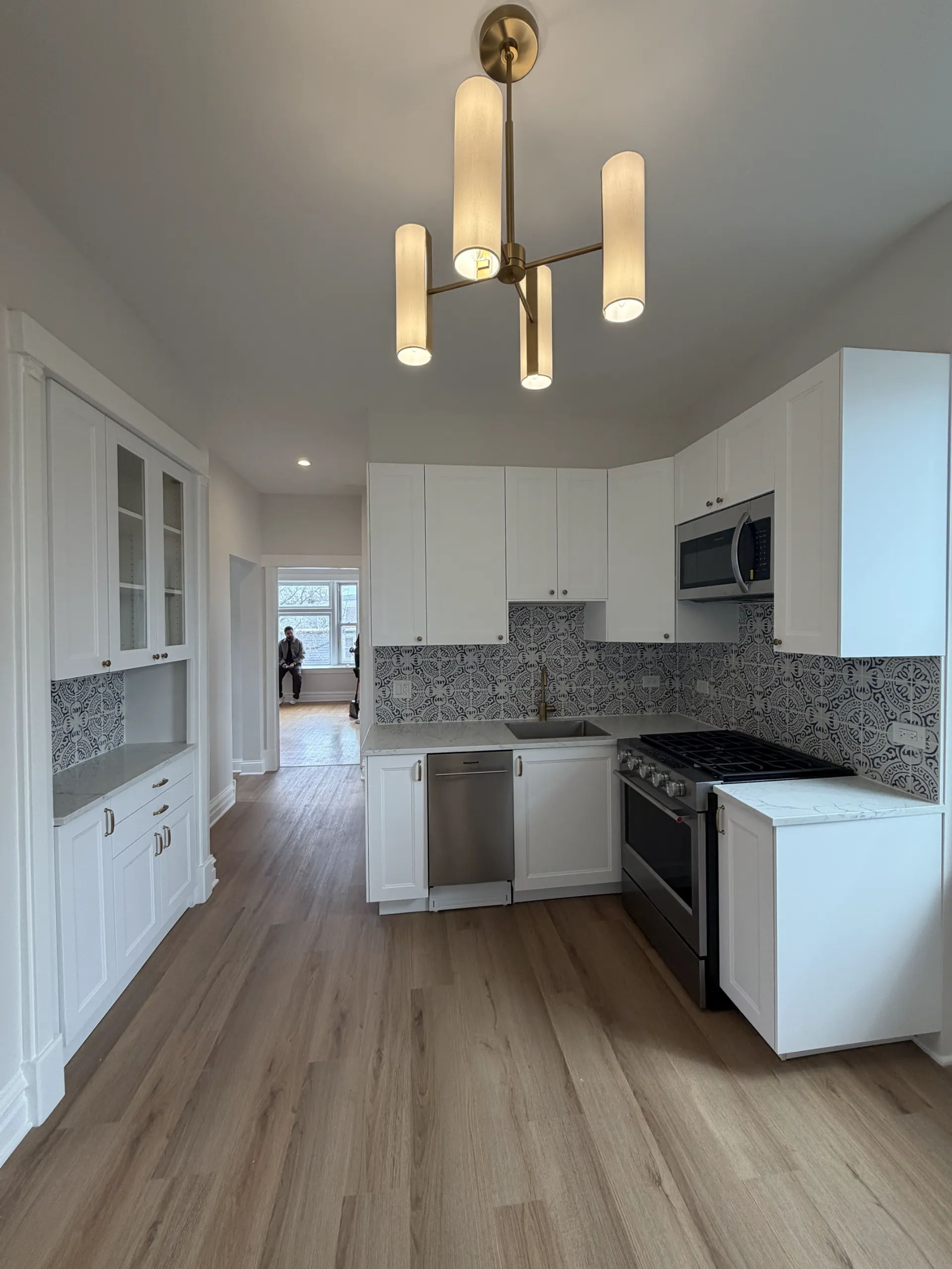 Open-concept white shaker kitchen remodel with Moroccan encaustic tile backsplash, brass chandelier, and quartz countertops in a Chicago Logan Square three-flat renovation by Assembly Squad